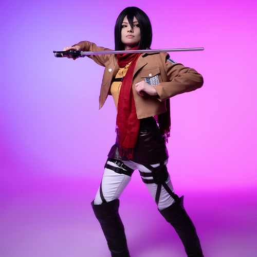 Mikasa Ackerman cosplay from Attack on Titan, standing in a strong combat stance with her blade ready, illuminated by a pink and purple backdrop