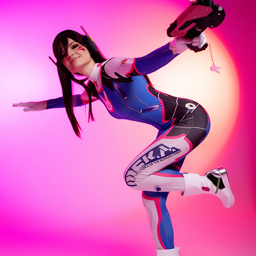 This energetic D.Va cosplay from Overwatch captures her playful yet determined personality. The vibrant pink and purple lighting creates a dynamic backdrop, highlighting the character's iconic blue, pink, and white bodysuit with detailed Korean Air Force insignias. The action pose with D.Va's signature light gun radiates confidence and energy, perfectly embodying this beloved hero from the game.