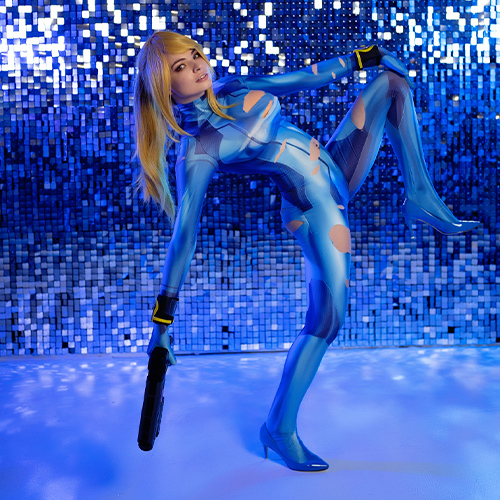 This stunning Zero Suit Samus cosplay captures the essence of the Metroid universe with its high-energy pose and vibrant aesthetic. The reflective blue mosaic background enhances the futuristic feel, perfectly complementing the detailed, form-fitting suit. The addition of the blaster and dynamic posture conveys Samus' agility and strength as a galactic bounty hunter. A dazzling interpretation of a beloved gaming icon!