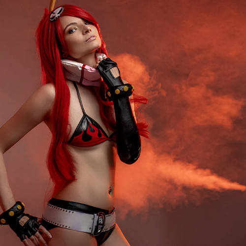 Captivating Yoko Littner cosplay from Tengen Toppa Gurren Lagann, highlighting her flame-patterned bikini, signature red hair, and confident pose against a smoky orange background. Perfect for fans seeking Yoko Littner cosplay ideas or anime-inspired photoshoots