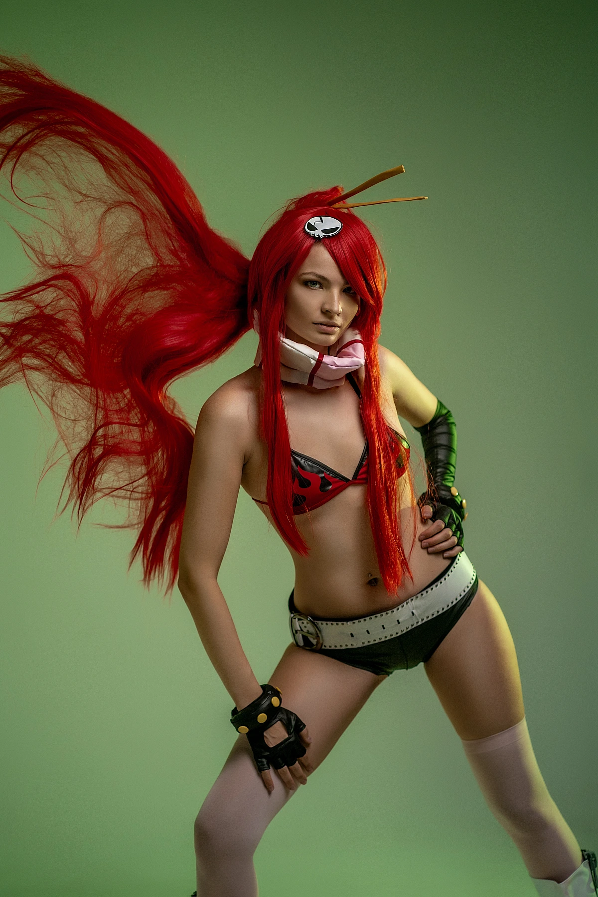 Yoko Littner cosplay dynamic motion shot, hair flip mid-swing, green studio background, flame bikini top, belt, black gloves, action anime photography