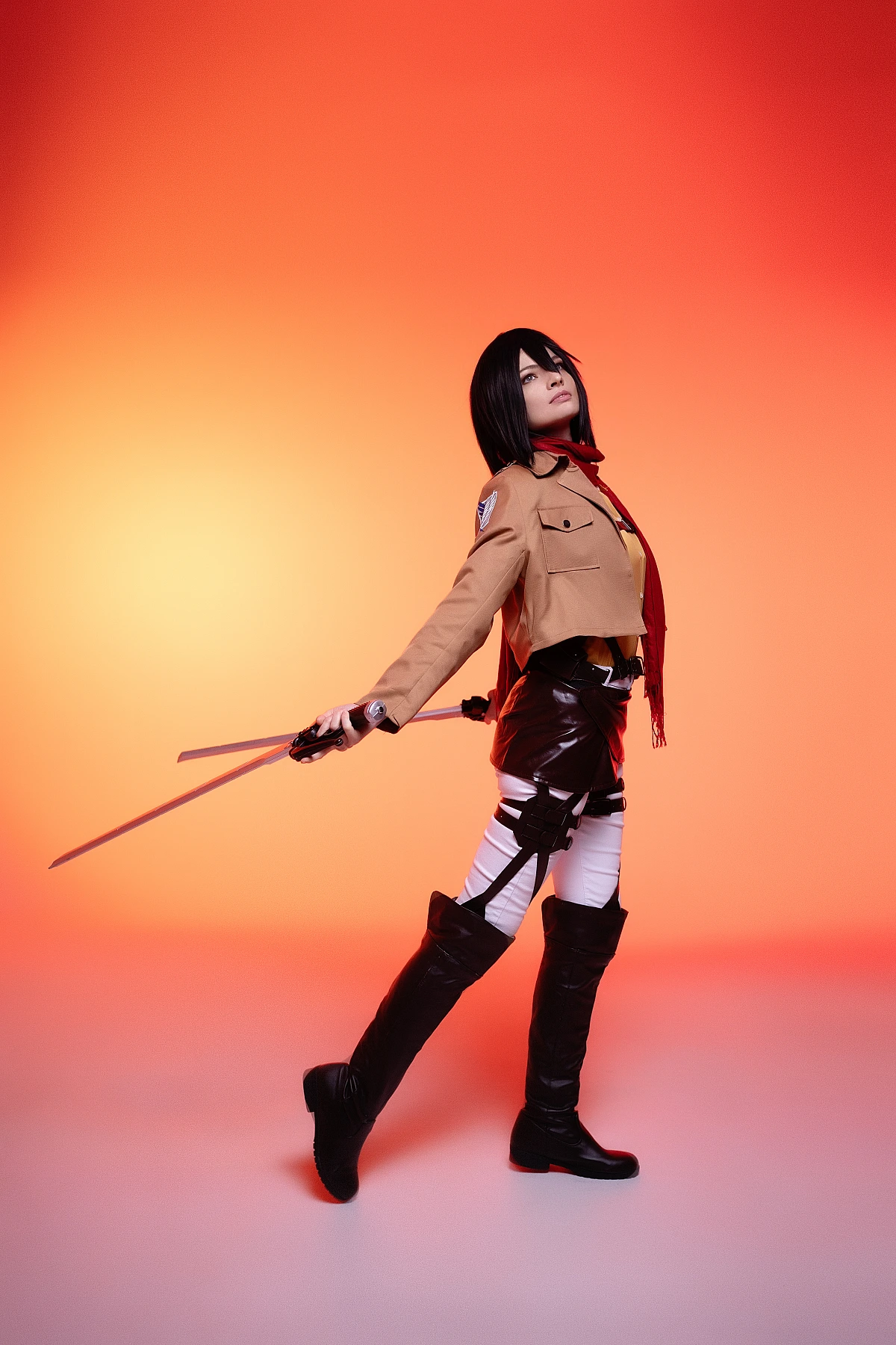 mikasa ackerman cosplay side profile with lowered dual blades and red scarf drape against warm orange backdrop