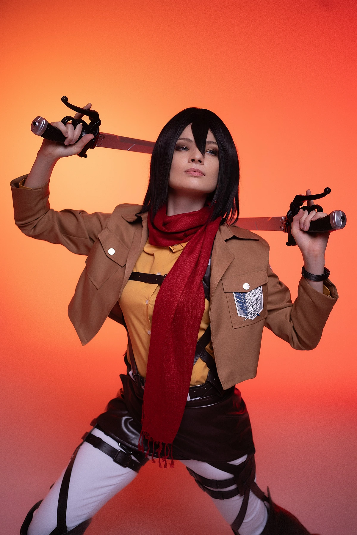 mikasa ackerman cosplay symmetric dual blade guard pose with odm harness straps against orange studio background