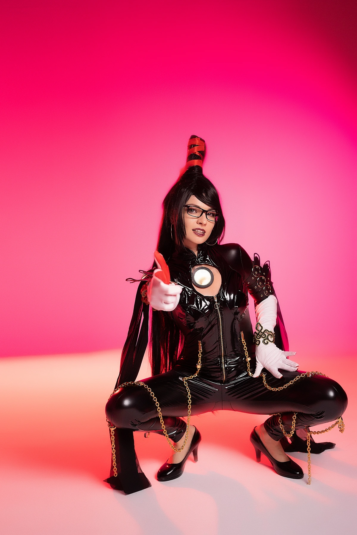 Bayonetta cosplay dynamic low squat with pointing gesture by Neka-Chi, glossy black bodysuit, intense neon pink backdrop
