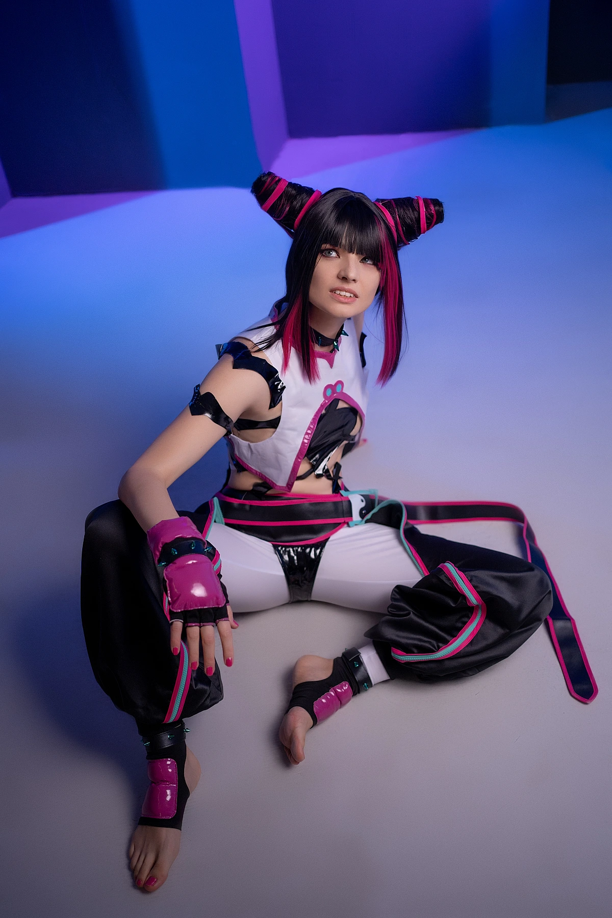 Juri Han cosplayer sitting on studio floor, barefoot, cool blue-violet neon lighting, relaxed pose, horn buns, Street Fighter