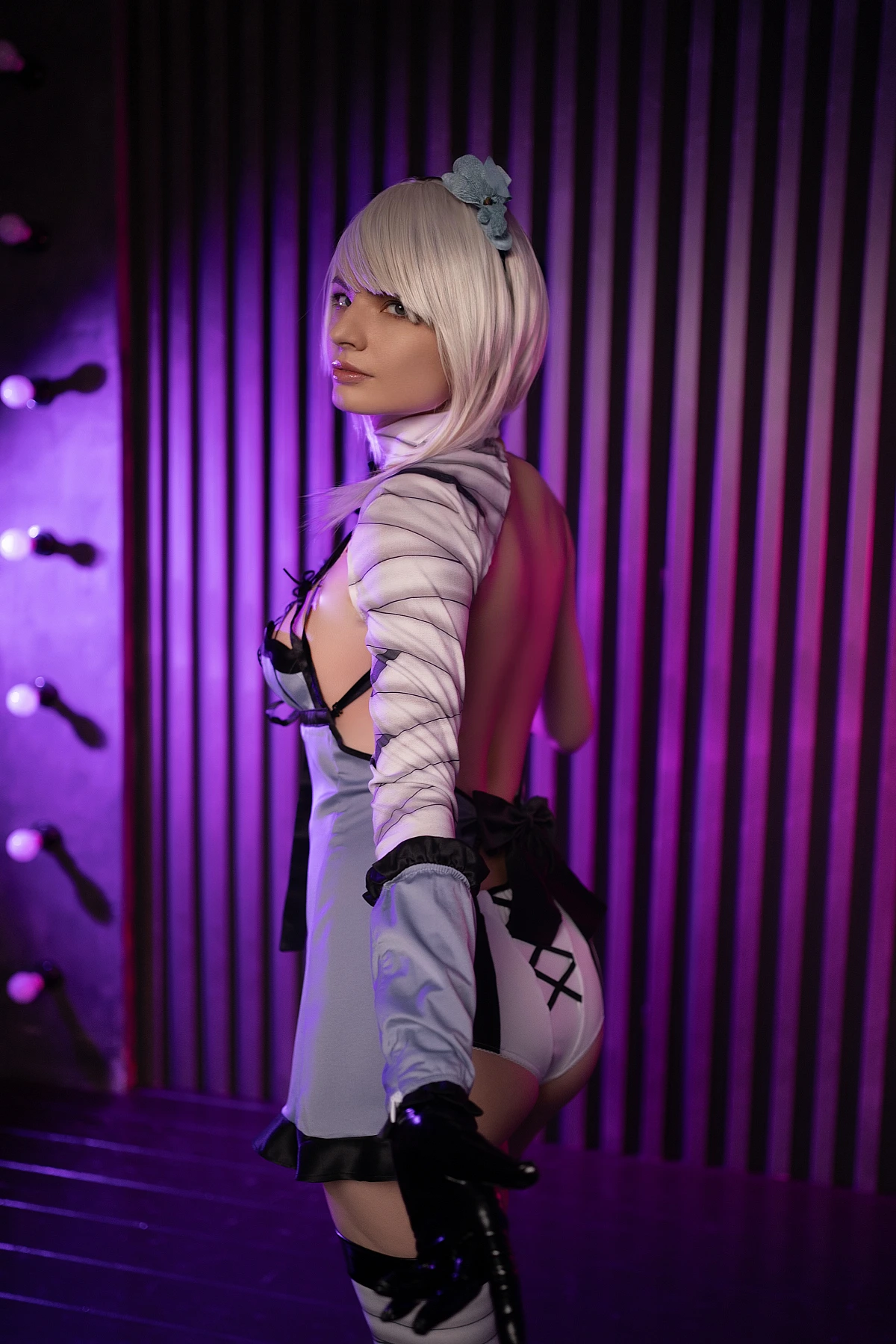 Kaine NieR Replicant cosplay back view silhouette with purple neon lighting, short white hair, glossy gloves, and striped wall background