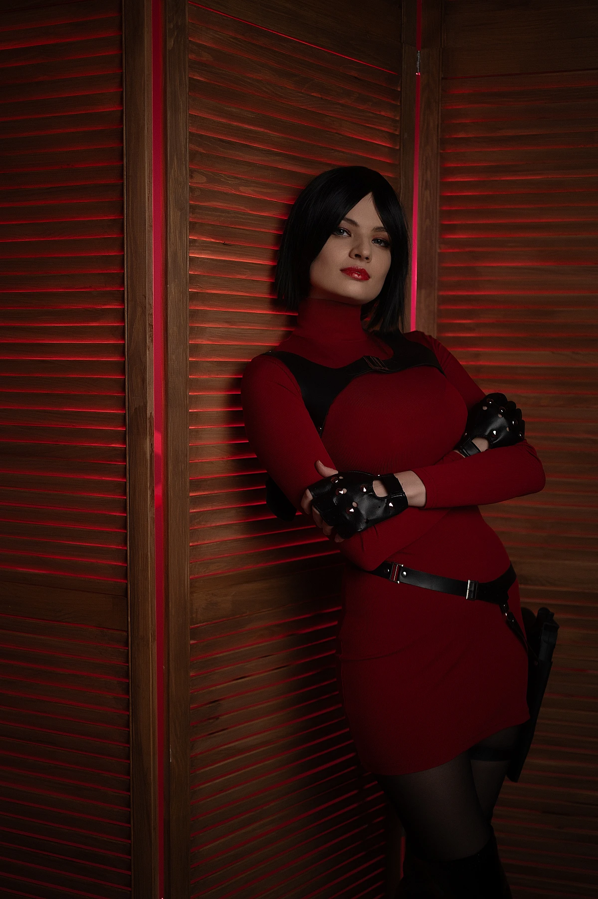 Ada Wong cosplay leaning wooden panels crossed arms red outfit black gloves warm red backlight