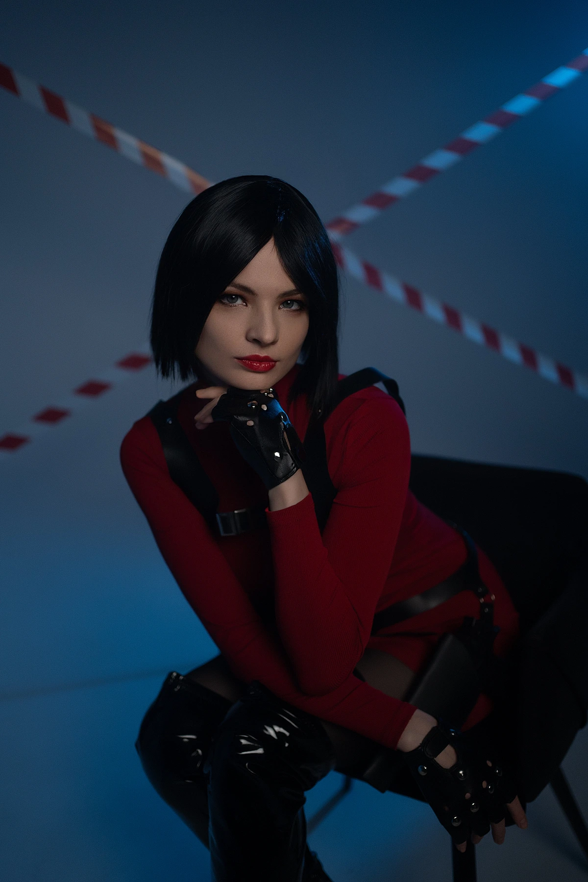 Ada Wong cosplay intimate portrait seated gloved hand chin red outfit blue studio lighting