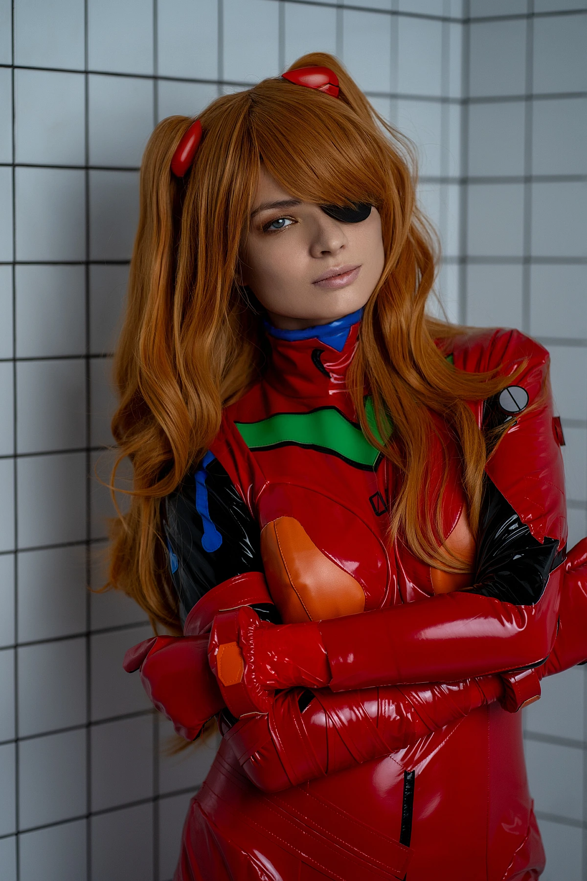 Intimate close portrait of Asuka Langley cosplay with folded arms, glossy red plugsuit texture visible, eyepatch and calm expression against tiled studio wall