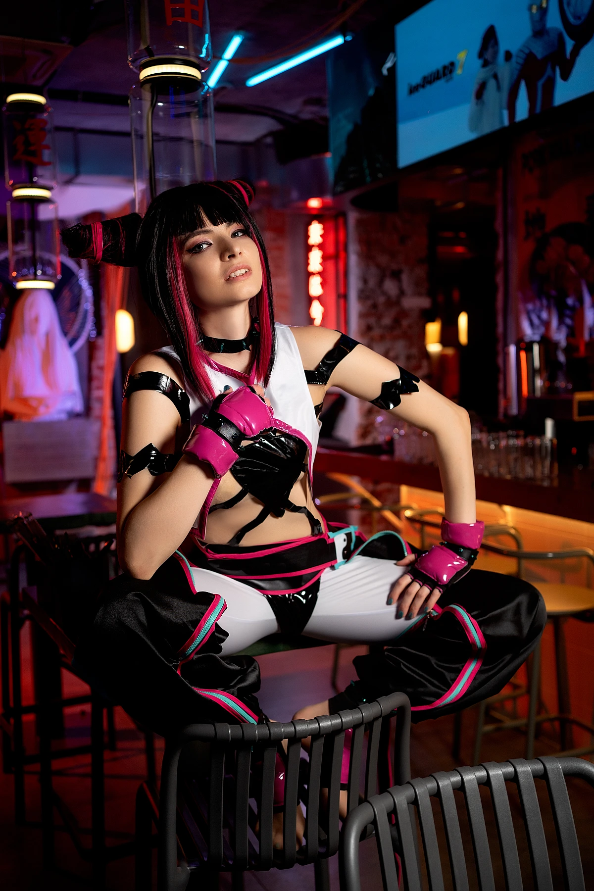 Juri Han Street Fighter cosplay crouching on chair in neon bar with glossy black costume, red neon lighting and industrial reflections
