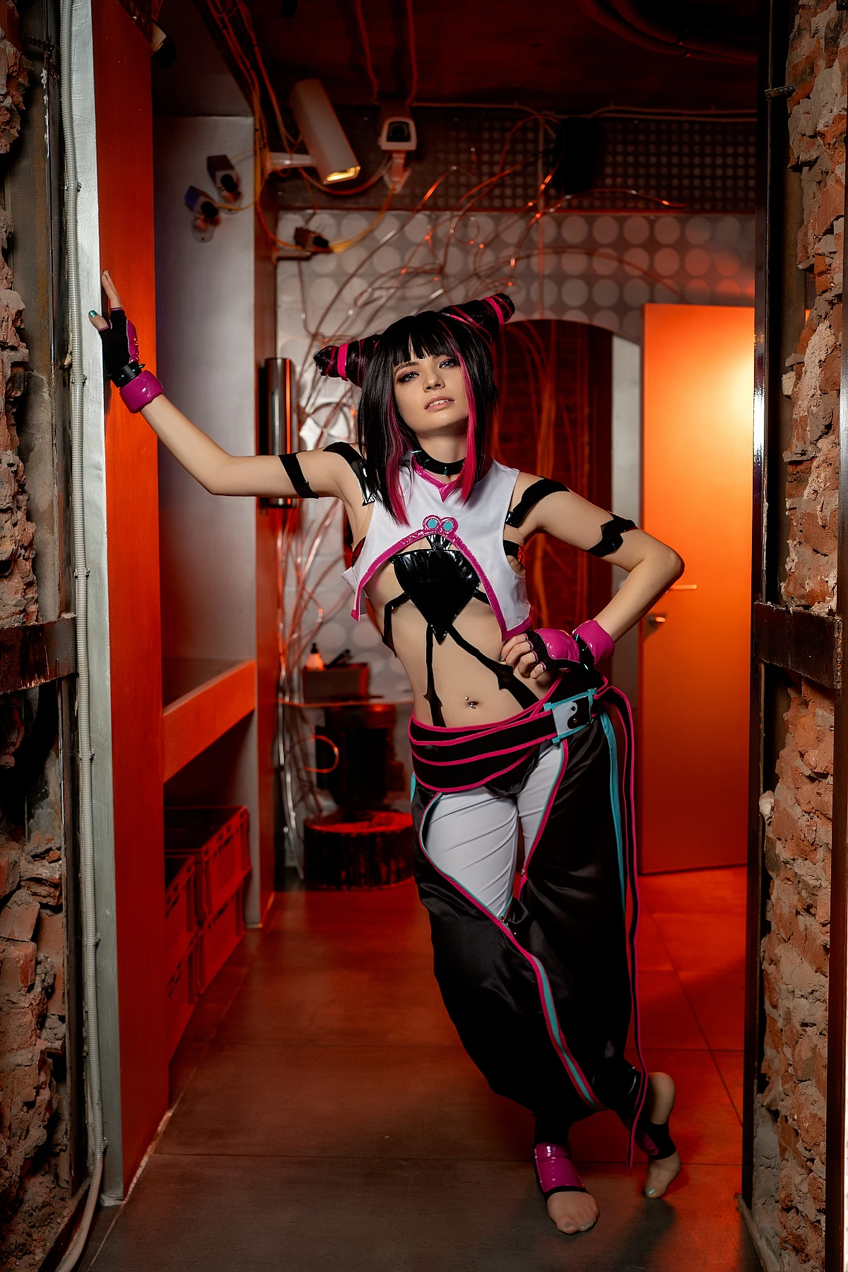Juri Han cosplay barefoot in neon-lit industrial corridor, leaning against brick wall with confident stance and red ambient lighting