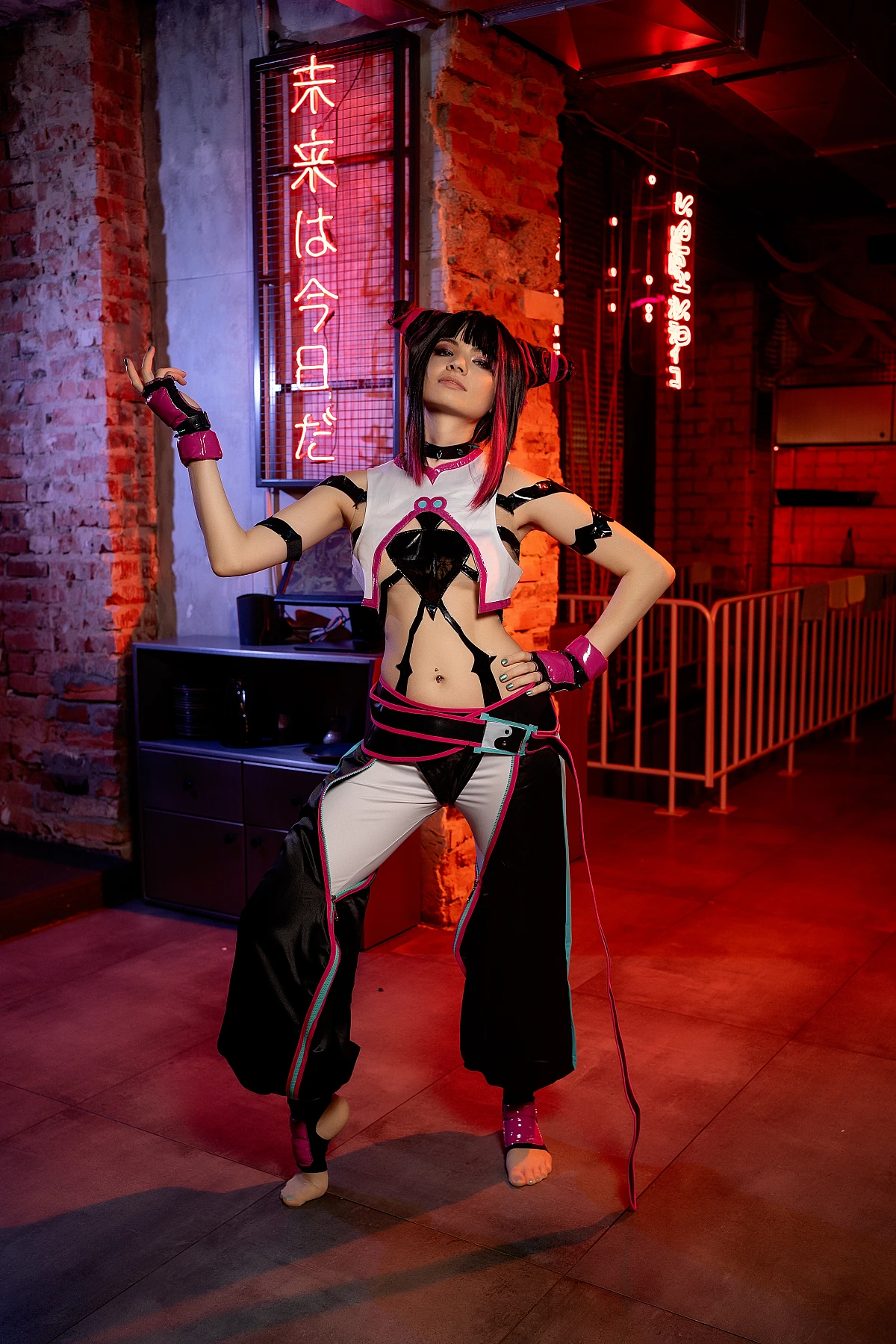 Juri Han cosplay in wide power stance with raised taunting hand, red neon lighting on brick walls, glossy costume accents