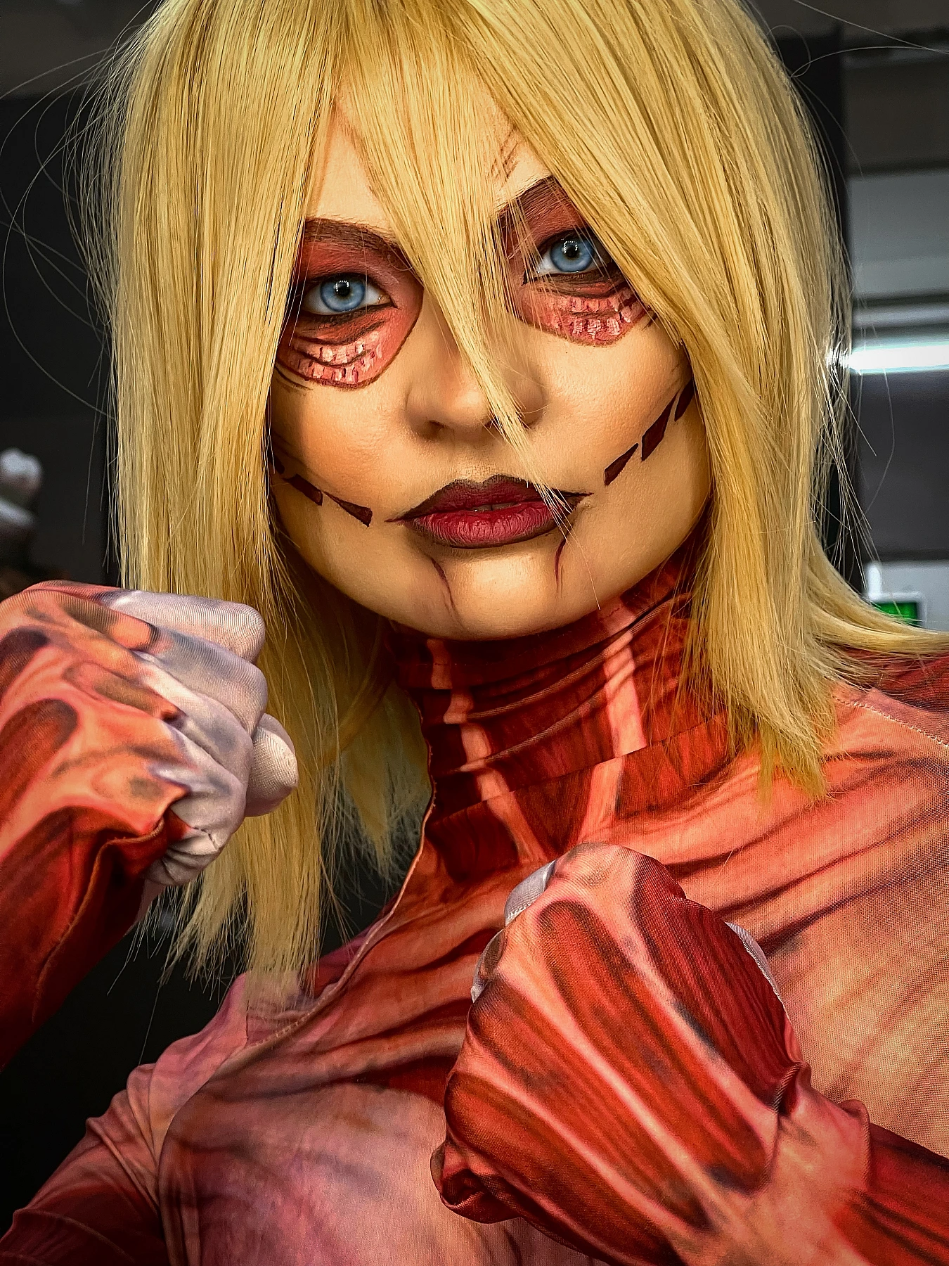 Annie Leonhart Female Titan cosplay close-up portrait with clenched fists, blue eyes, titan makeup, AOT cosplay photography