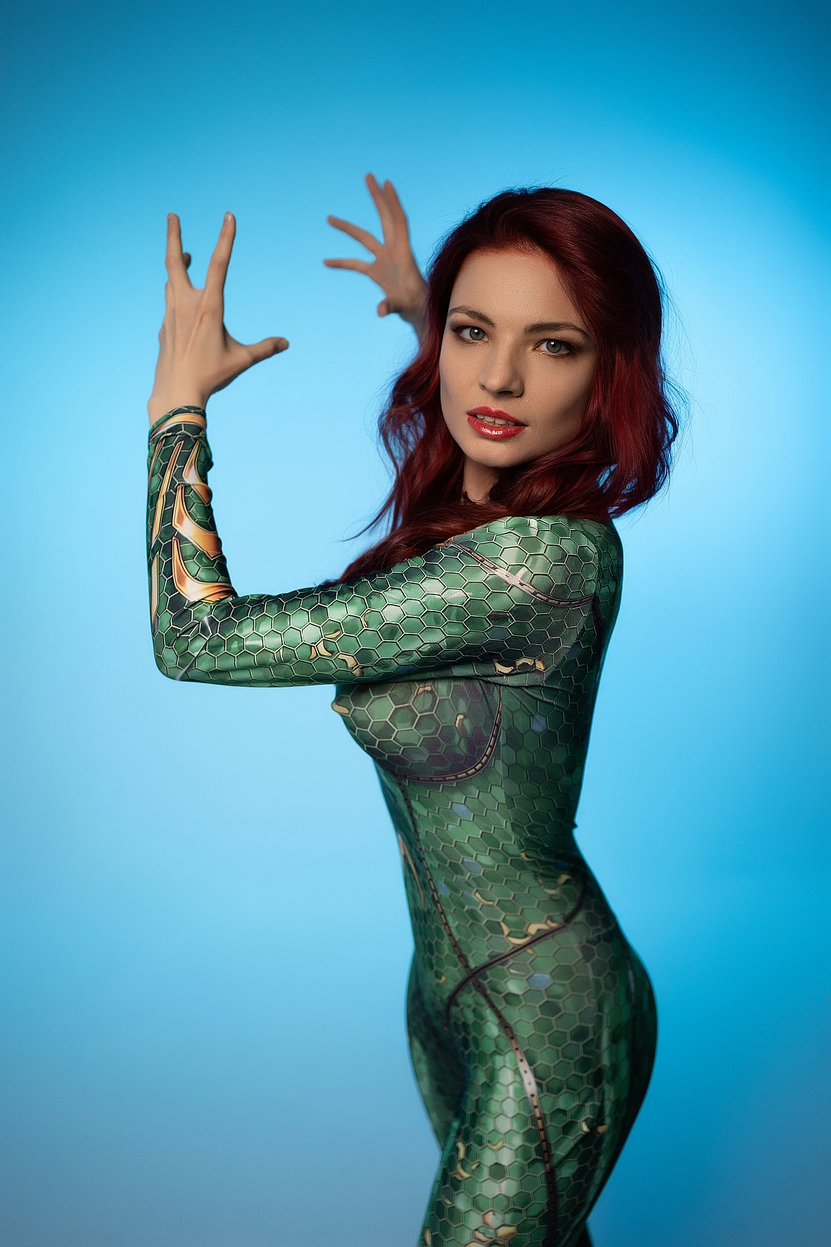 Side profile Mera cosplay with raised hands gesturing in emerald scale bodysuit