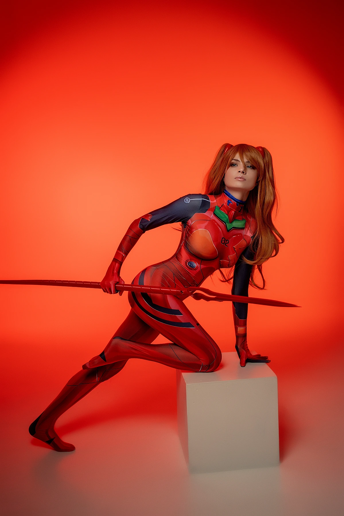 Asuka Langley cosplay leaning low on cube holding weapon in crimson lighting