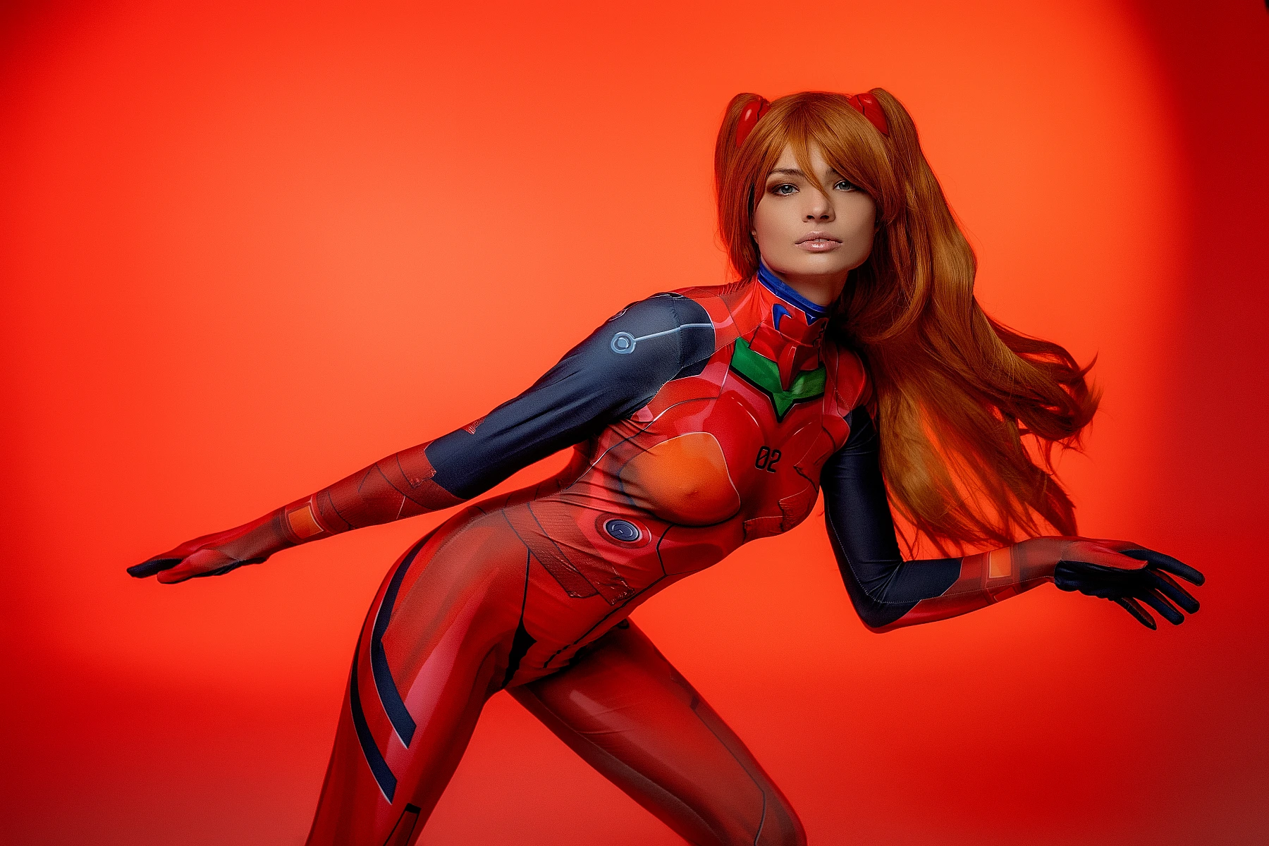 Asuka Langley cosplay leaning sideways in red plugsuit with flowing orange hair