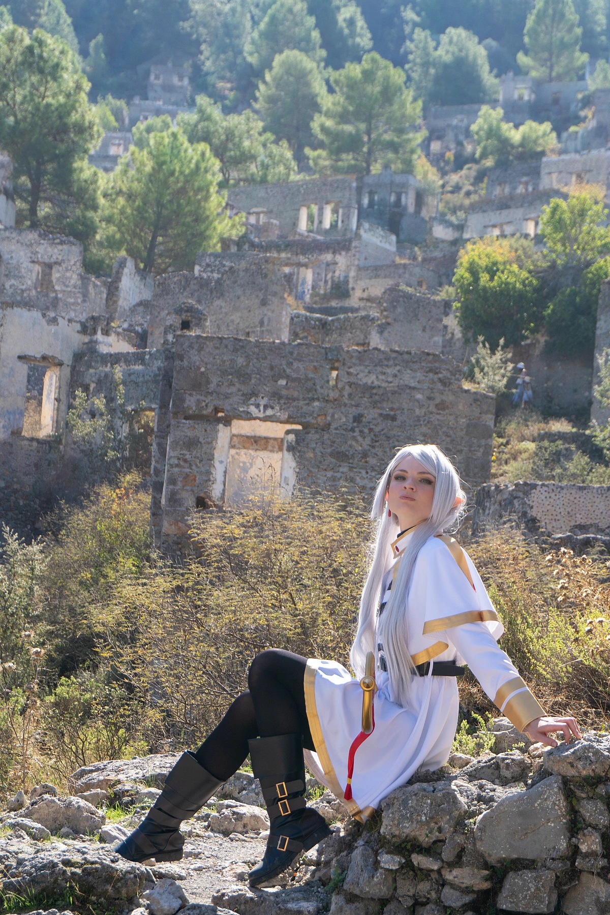 Frieren cosplay seated stone wall silver hair elf ears white gold dress hillside ruins landscape natural light Sousou no Frieren