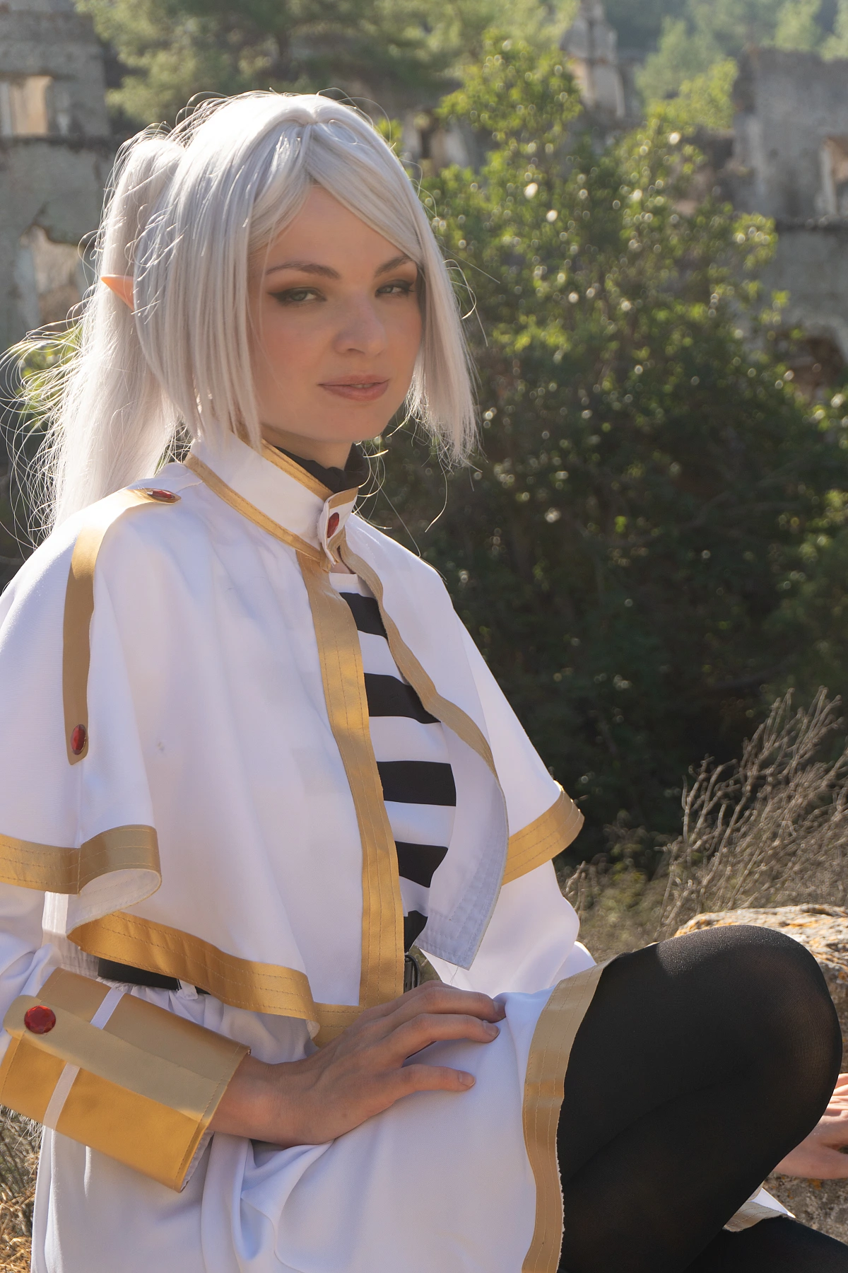 Frieren cosplay seated portrait composed expression silver hair elf ears white gold mage costume ruins background daylight