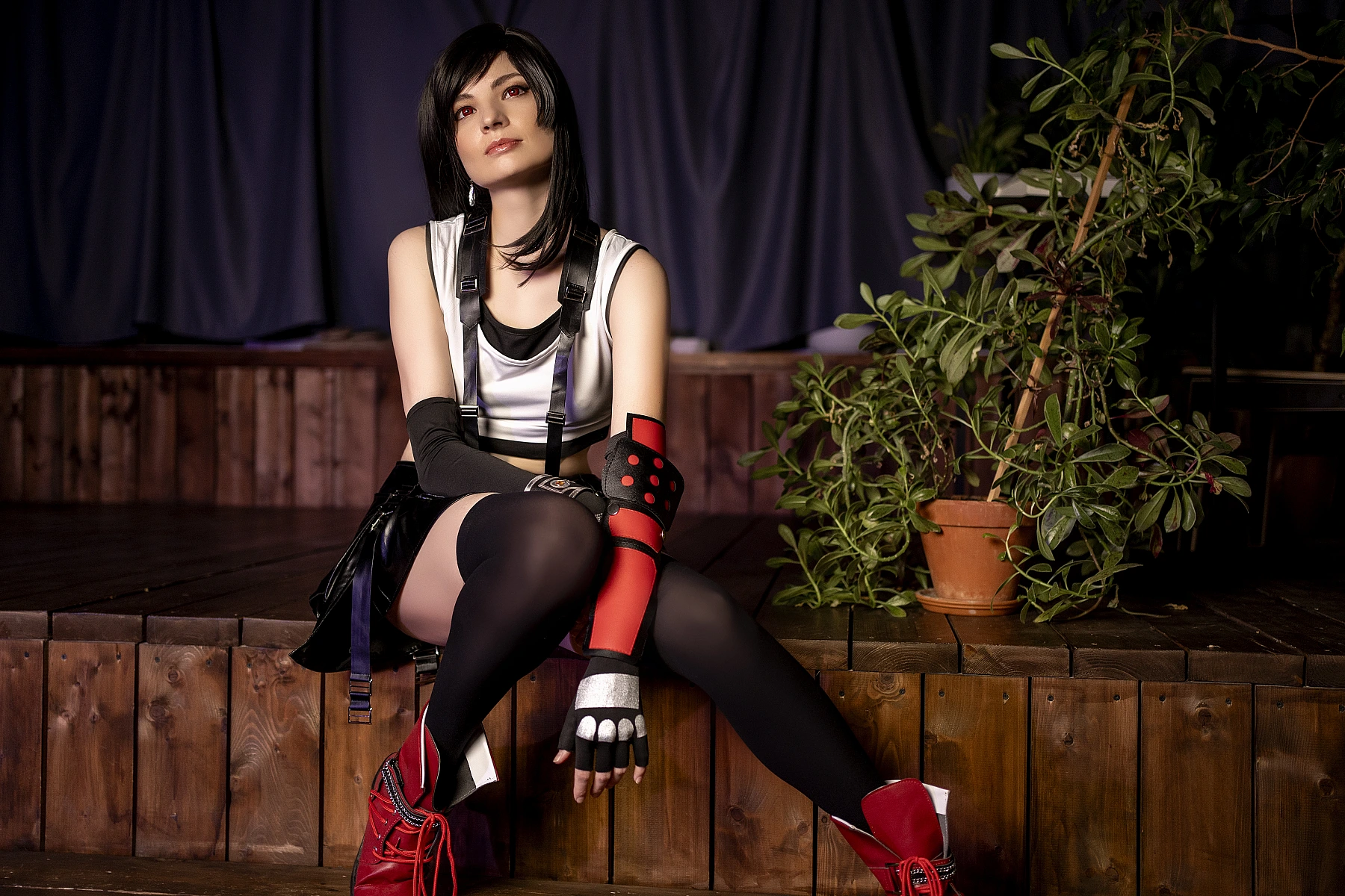 Tifa Lockhart cosplay relaxed seated recovery pose, muscular legs, FF7 costume with crop top skirt and suspenders, thigh-high stockings, red boots, soft lighting