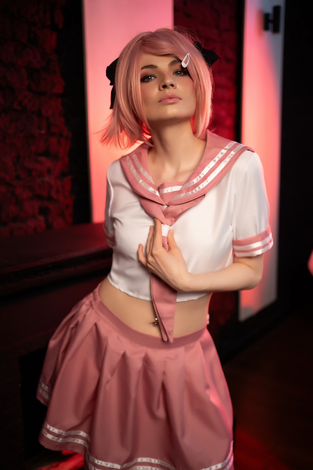 Astolfo trap cosplay portrait with hand near collar showing pink school uniform midriff and warm red lighting