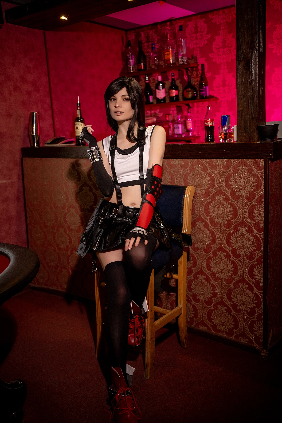 Tifa Lockhart cosplay seated on bar chair, bottle prop, elegant long legs, FF7 thigh-high stockings, red boots, atmospheric red bar lighting
