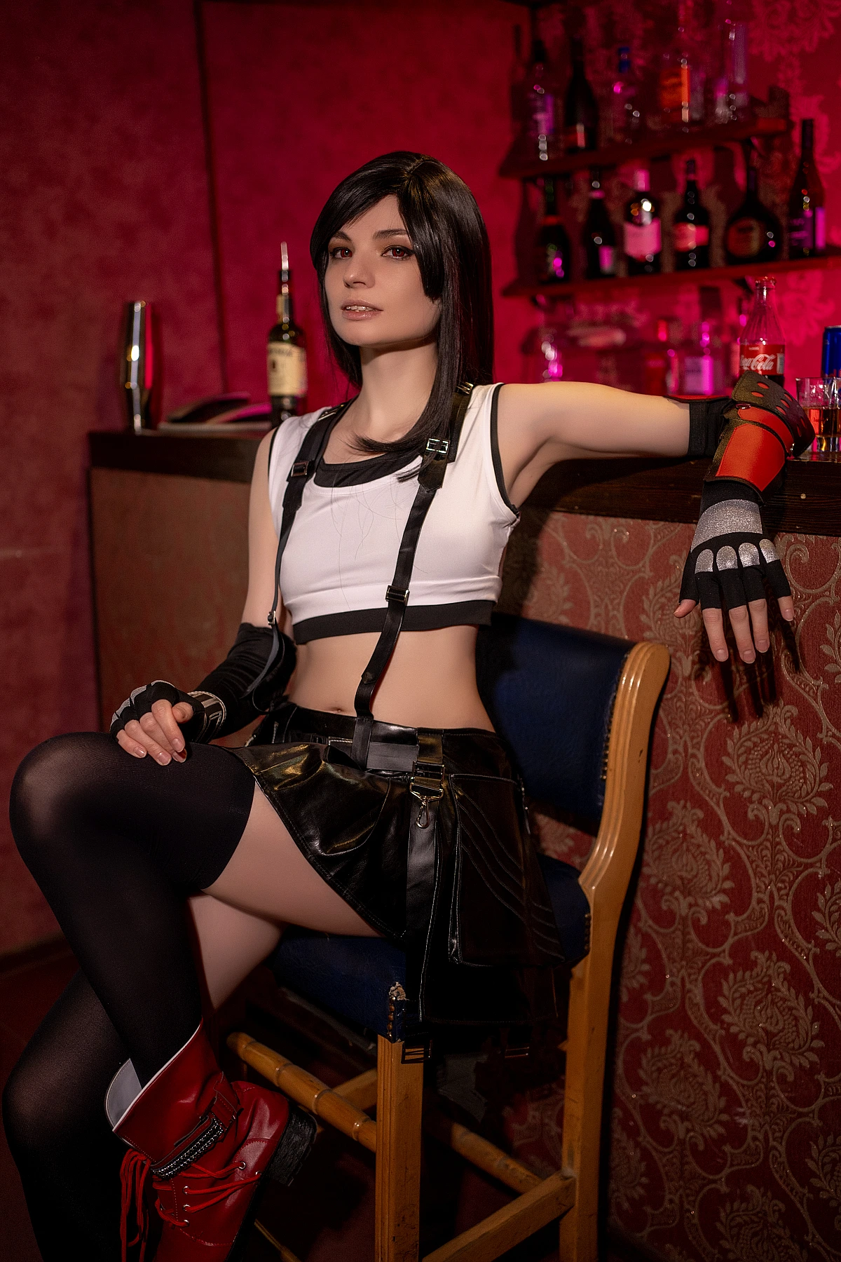 Tifa Lockhart classic cosplay 7th Heaven bar seated pose, white crop top, black skirt, suspenders, combat gloves, thigh-high stockings, red boots, warm red lighting