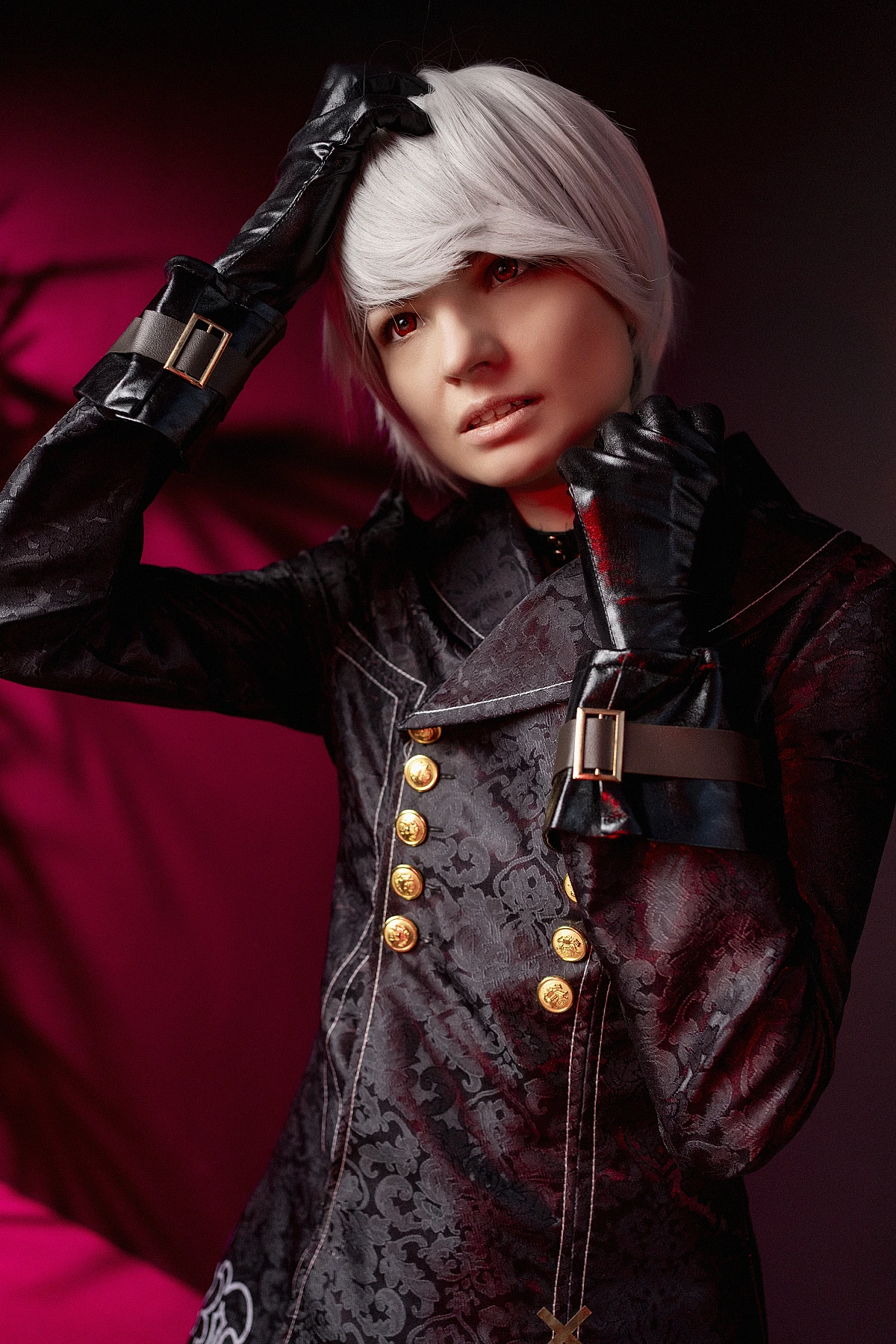 Close-up 9S cosplay with white hair and black YoRHa coat under red neon studio light.