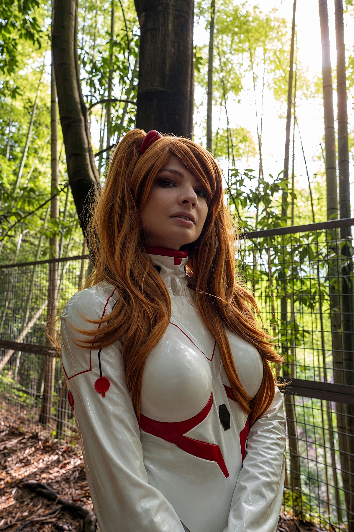 Asuka Langley cosplay portrait in a white Rebuild plugsuit with orange twin-tail wig standing in a bamboo grove