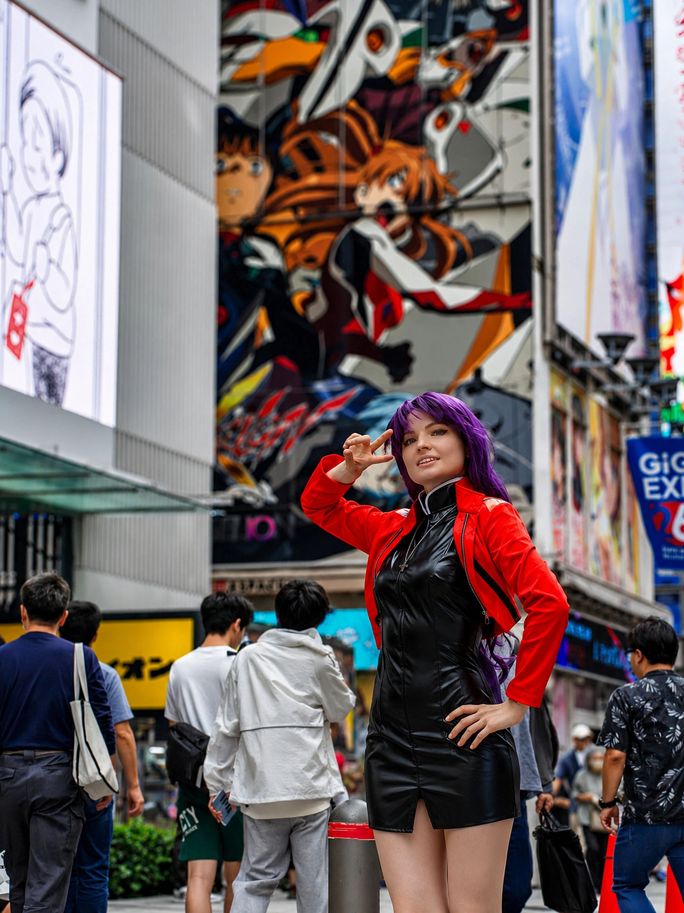 Misato Katsuragi cosplay posing in Akihabara near anime artwork and city crowds in a red jacket and black dress