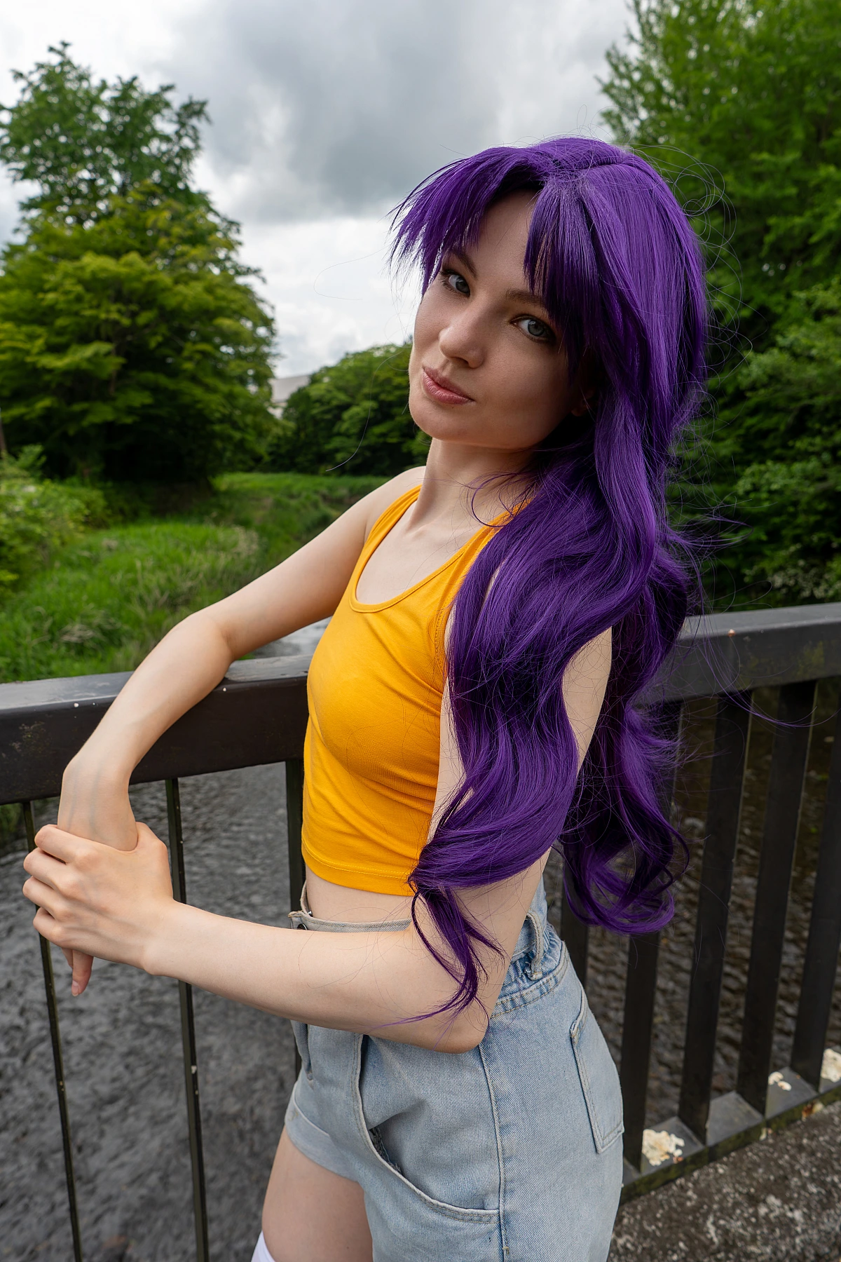 Misato Katsuragi casual cosplay leaning by a riverside bridge with long purple hair, yellow top and denim shorts