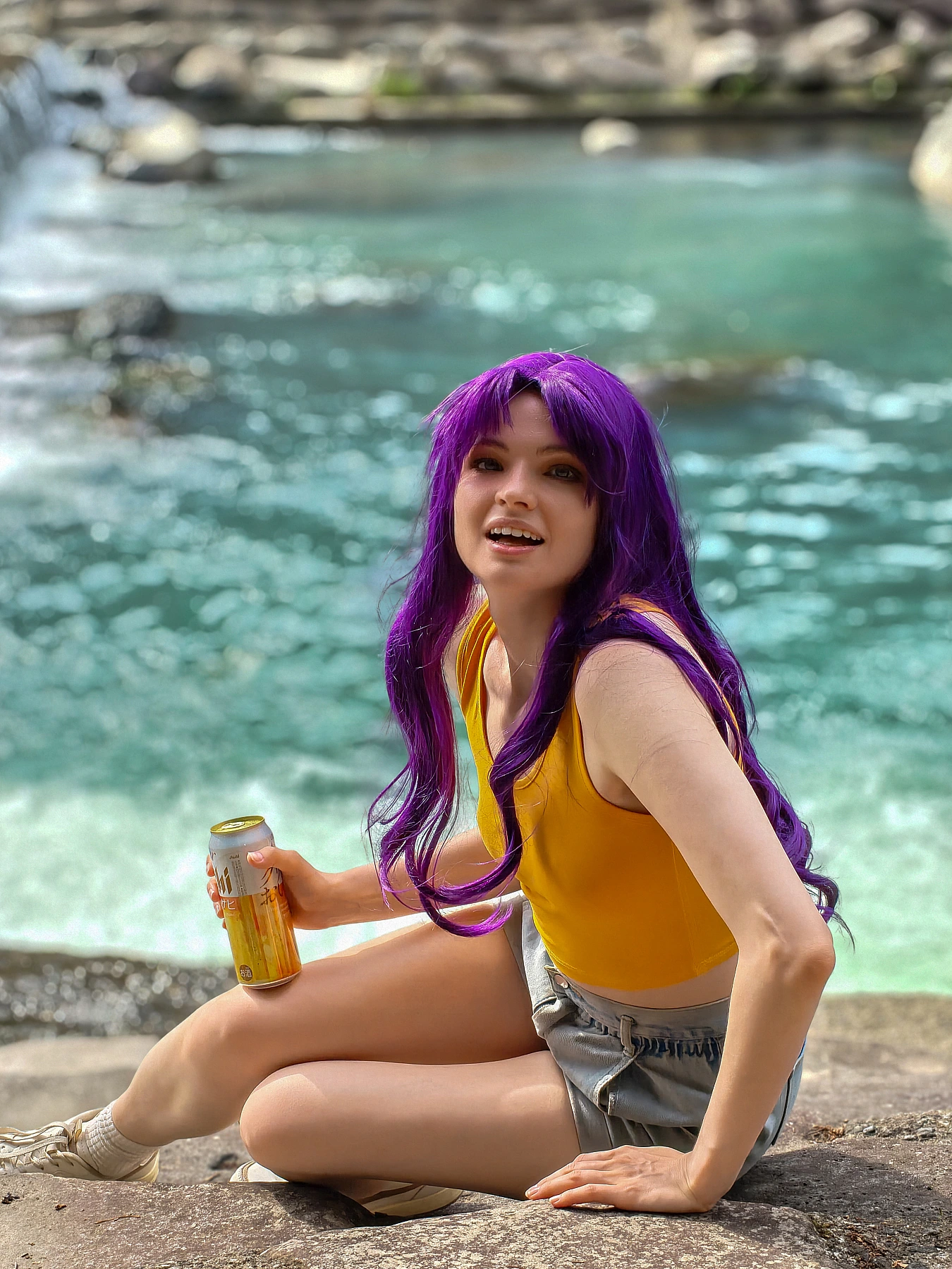 Misato Katsuragi casual cosplay seated by a clear river with purple hair, yellow top and denim shorts