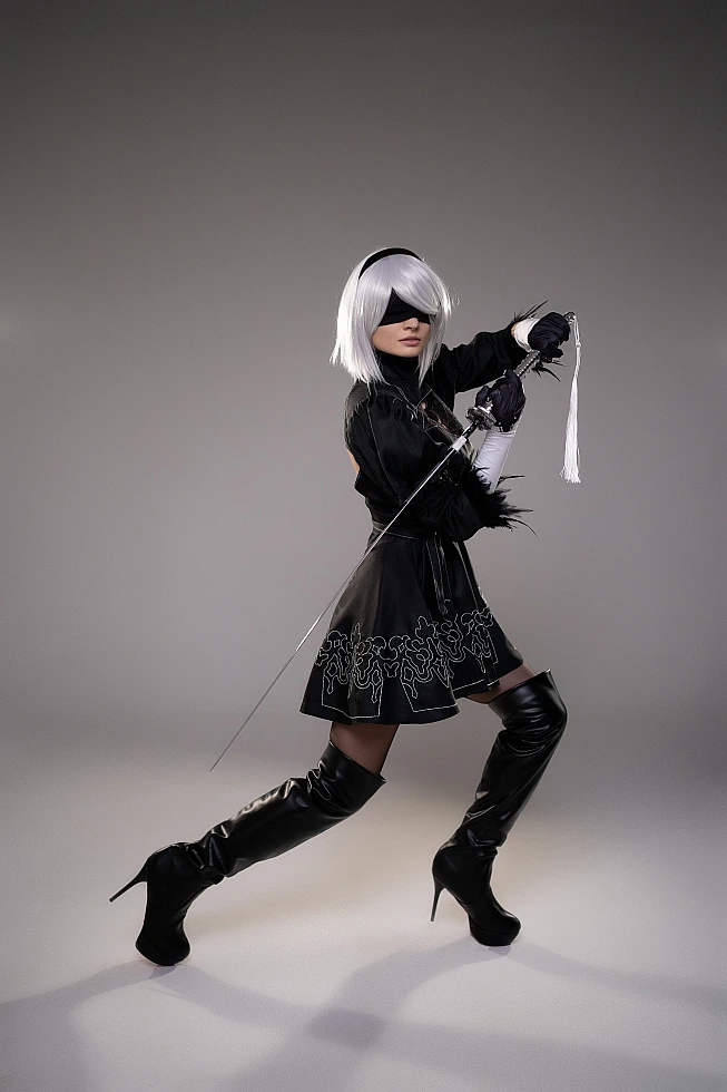 2B NieR Automata cosplay action pose with katana lunge attack, silver hair, blindfold, black dress, dynamic studio shot