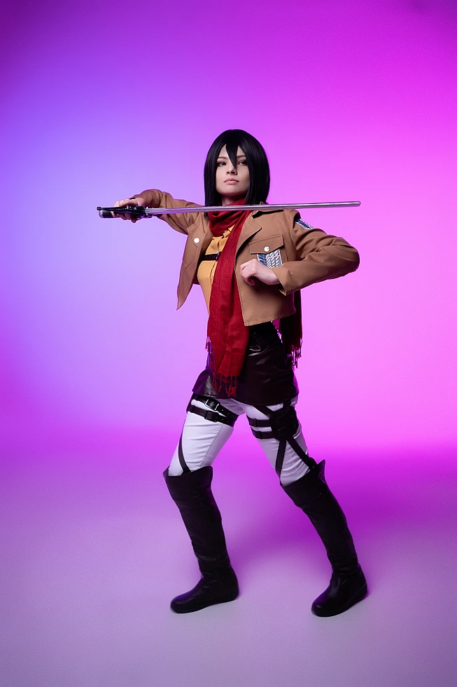 mikasa ackerman full-body cosplay with extended blade pose showing complete survey corps costume against purple-pink backdrop