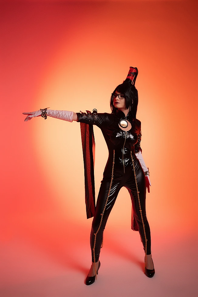 Bayonetta cosplay standing with commanding outstretched arm, glossy black bodysuit, red-orange gradient backdrop by Neka-Chi