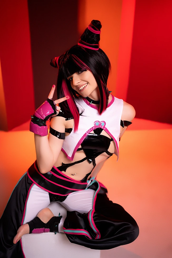 Juri Han cosplayer smiling on white cube, barefoot, playful hand gesture, warm orange neon columns, horn buns, Street Fighter