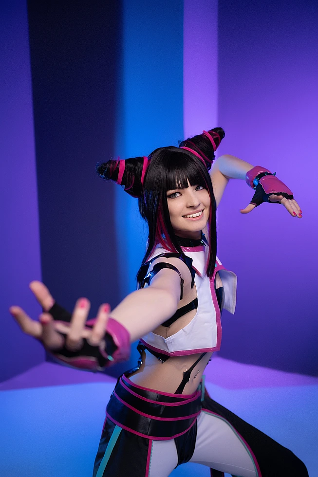 Juri Han cosplayer leaning forward with hand reaching toward camera, blue-violet neon studio background, dynamic action pose, Street Fighter