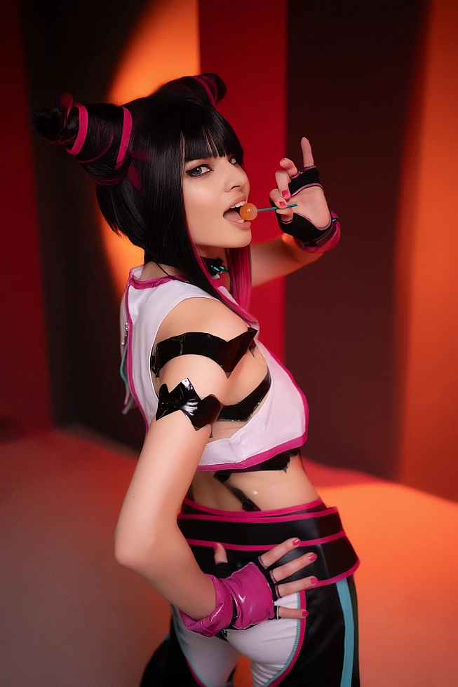 Juri Han cosplay side profile with lollipop near lips, warm orange-red neon studio background, glossy strap costume, horn buns, Street Fighter