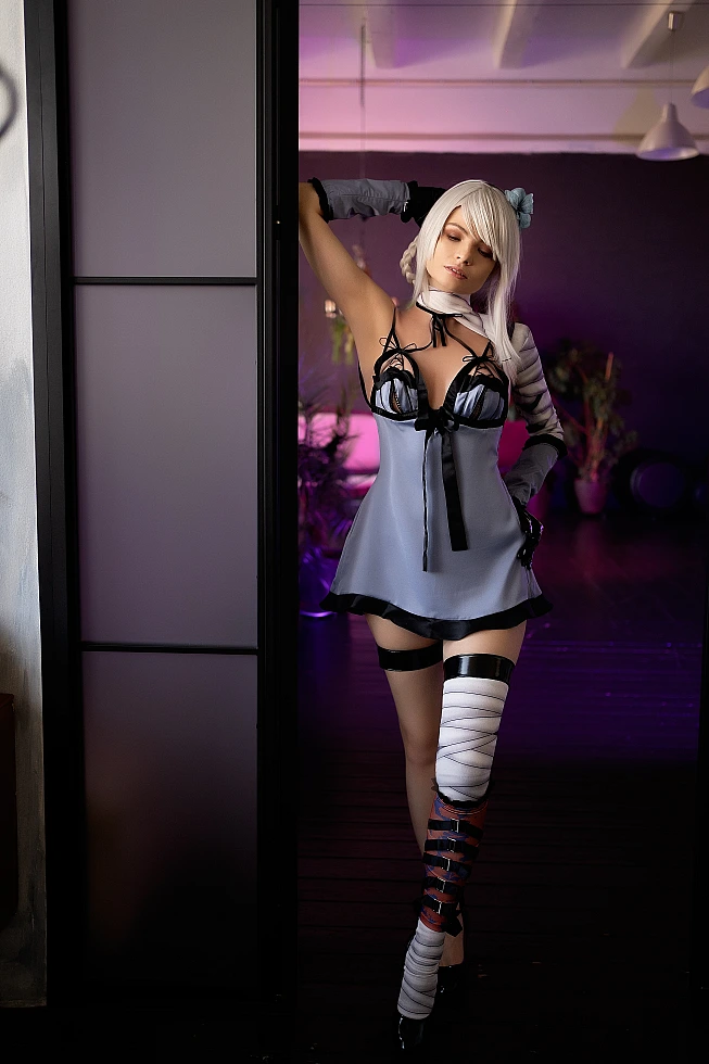 Kaine NieR Replicant cosplay standing in doorway frame with raised arm pose, silver hair, bandaged leg, muted purple-pink studio glow