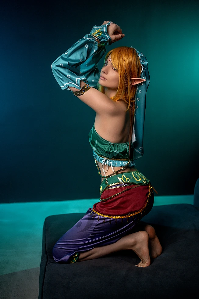 Gerudo Link cosplay kneeling profile adjusting veil with teal backdrop
