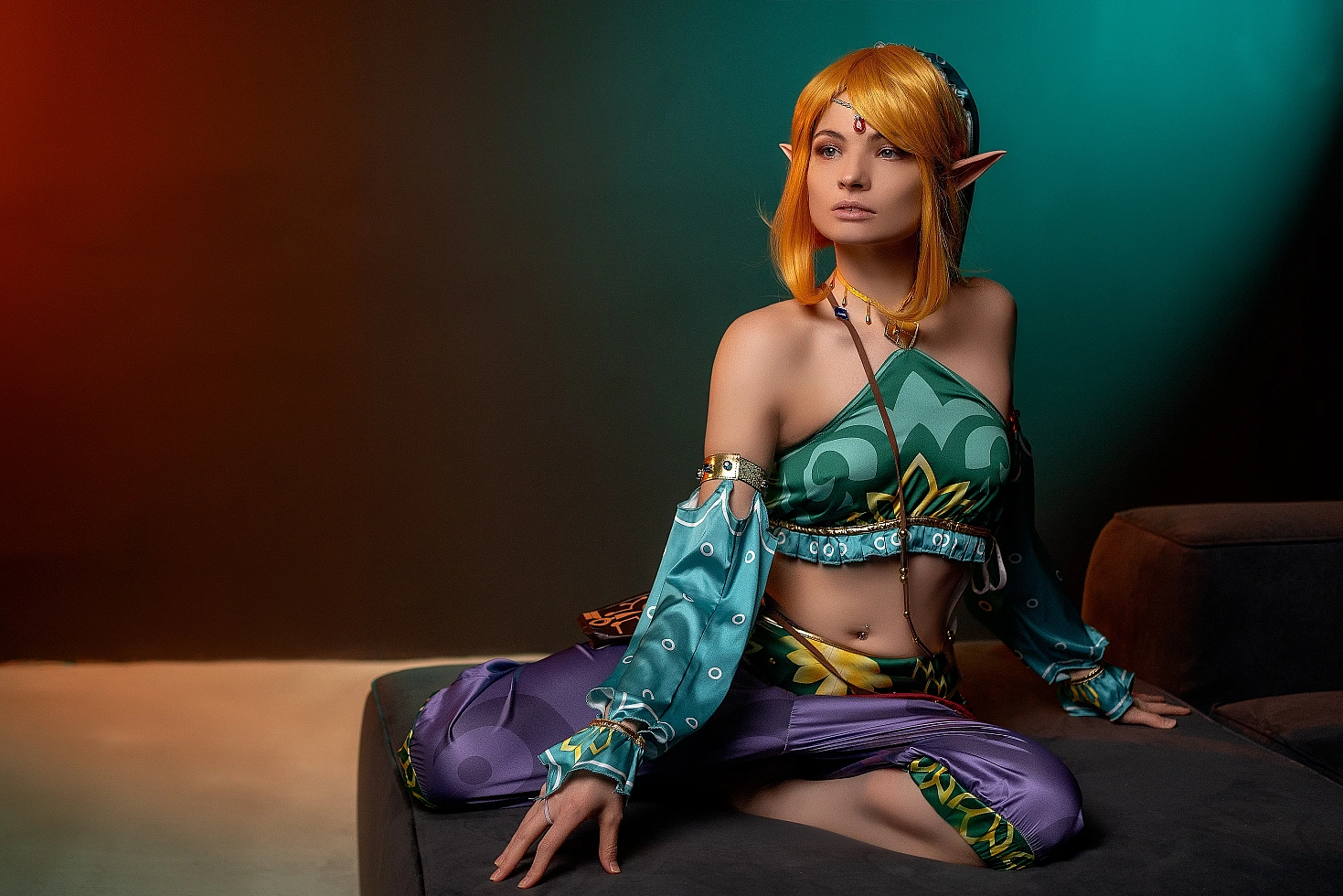 Gerudo Link cosplay seated on ottoman with teal-amber gradient lighting
