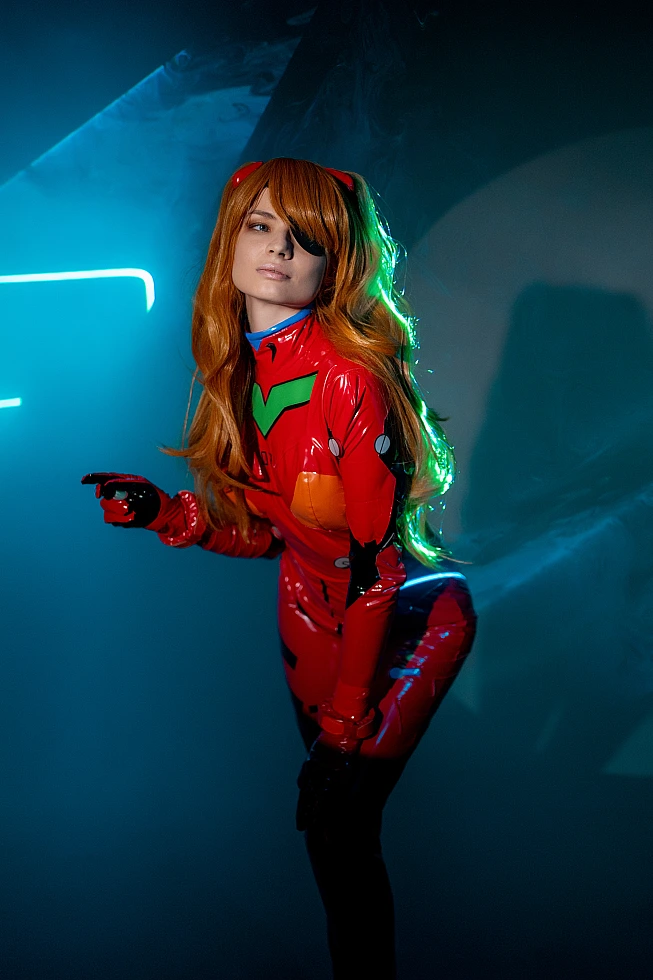 Moody side profile Asuka Langley plugsuit cosplay with subtle pointing gesture, soft neon edge light on red suit, flowing orange hair in dark studio