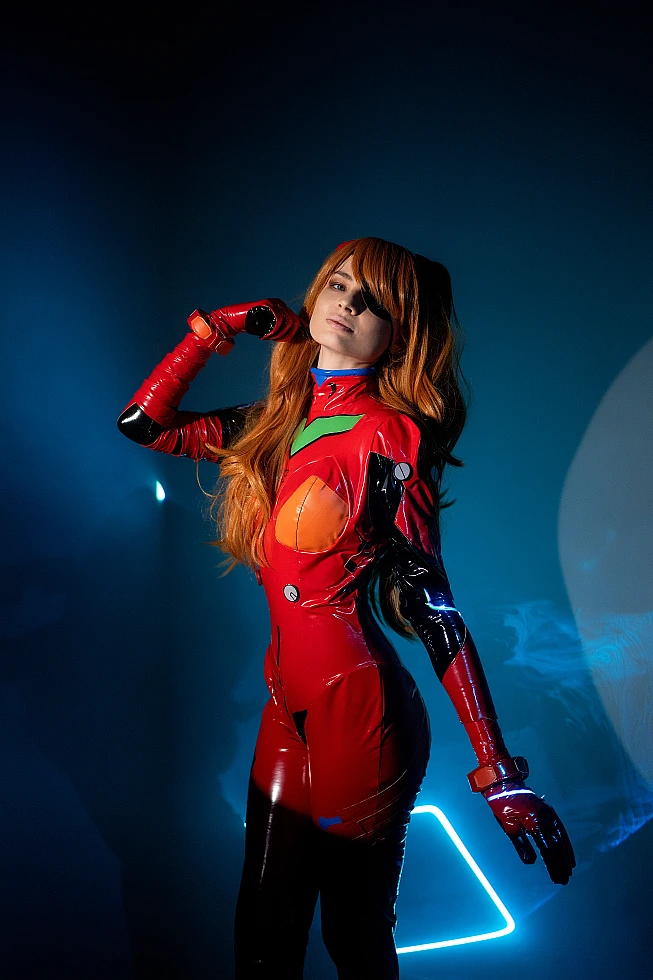 Asuka Langley cosplay in red plugsuit with geometric neon light shapes behind, confident standing pose in atmospheric dark studio with haze