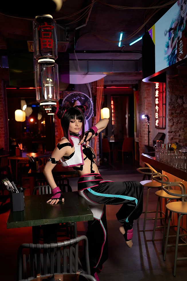 Juri Han cosplay leaning back on bar table with one leg raised, creating diagonal line, warm neon reflections throughout