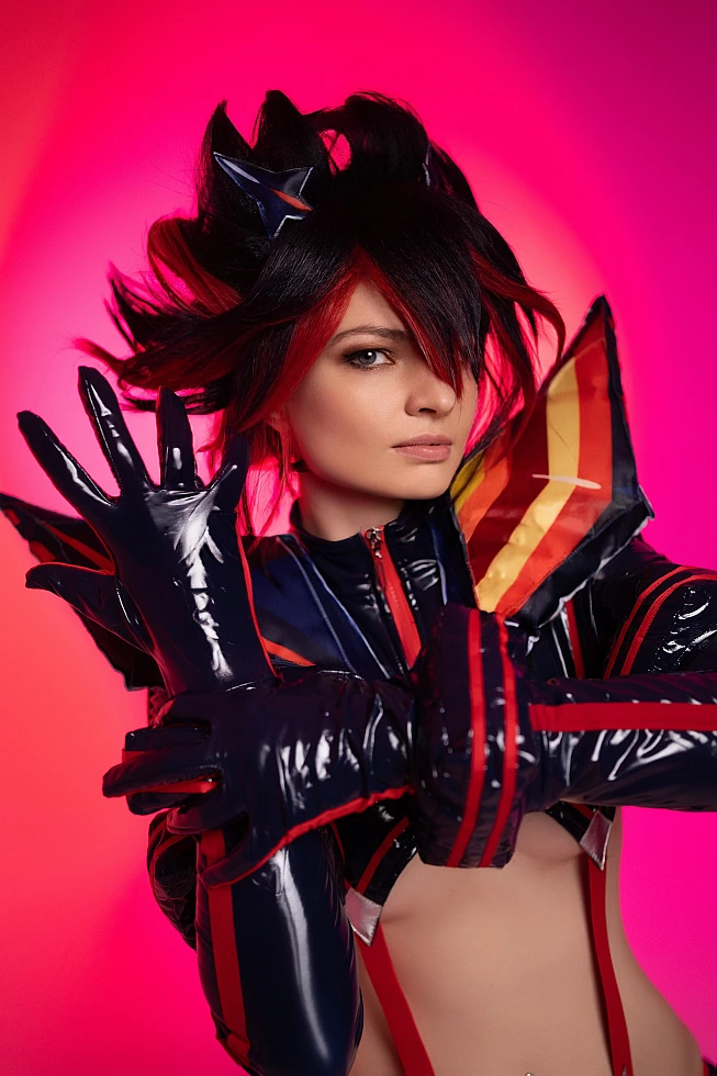 Ryuko Matoi cosplay intense close portrait raised gloved hand neon crimson pink studio background glossy Senketsu details Kill la Kill