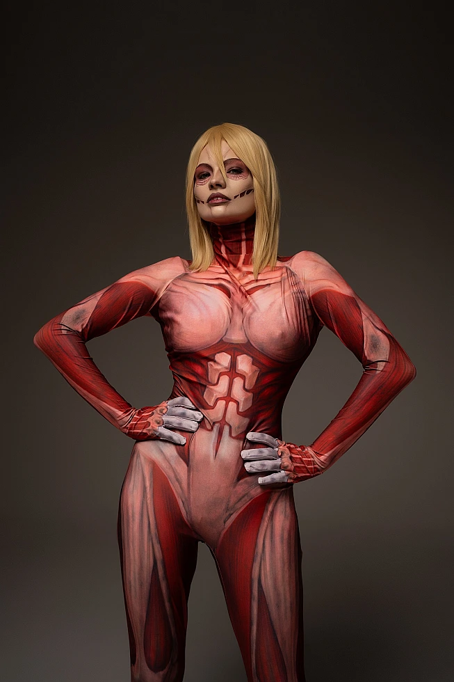 Female Titan cosplay hands on hips, Annie Leonhart dominance stance, anatomical muscle bodysuit, dark studio AOT cosplay