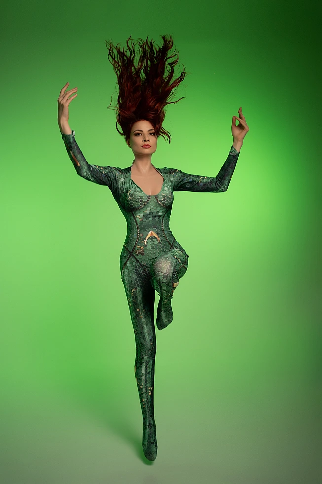 Mera cosplay floating pose with raised arms and lifted leg against vivid green backdrop