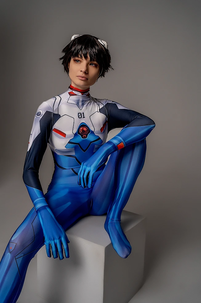 androgynous Shinji Ikari cosplay seated on cube, blue Eva bodysuit, bare feet, anime crossplay photoshoot, neutral studio