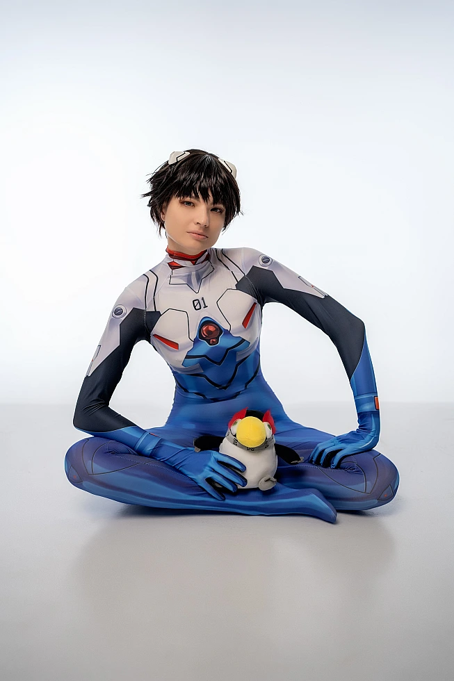 androgynous Shinji Ikari cosplay floor pose with Pen Pen penguin plush, blue bodysuit, anime crossplay photoshoot
