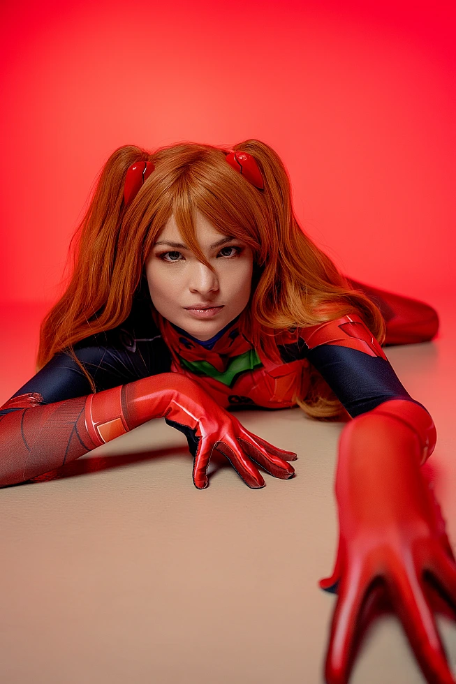 Close-up Asuka Langley cosplay in red plugsuit reaching toward camera with intense gaze