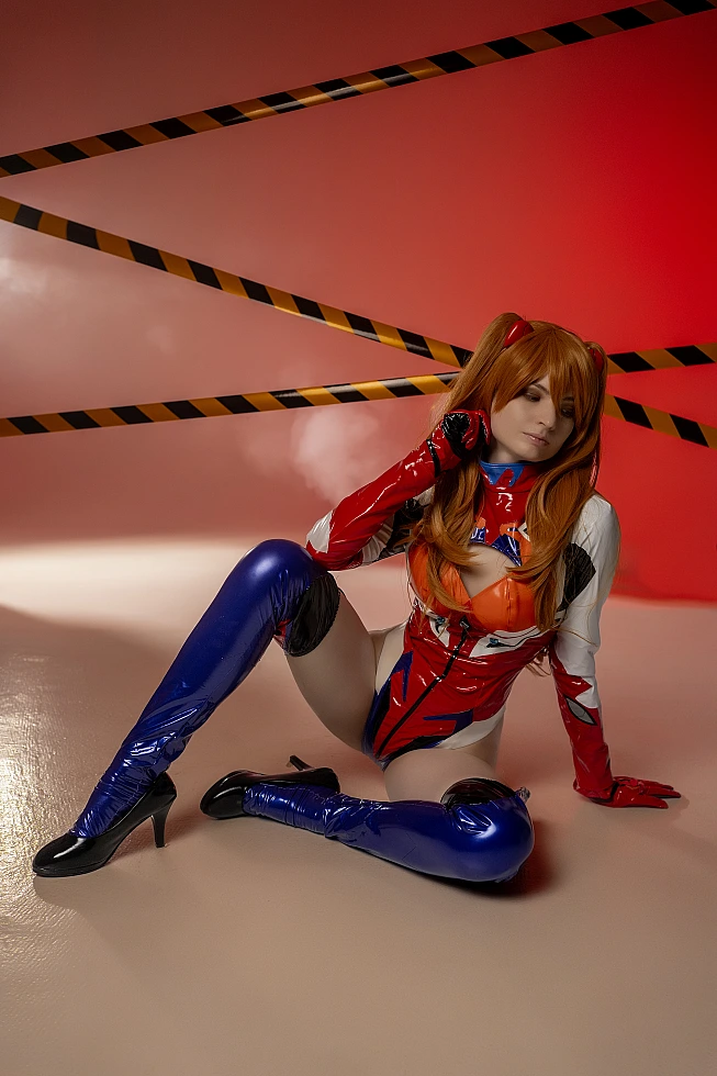 Asuka seated floor pose cosplay with latex stockings and red studio lighting